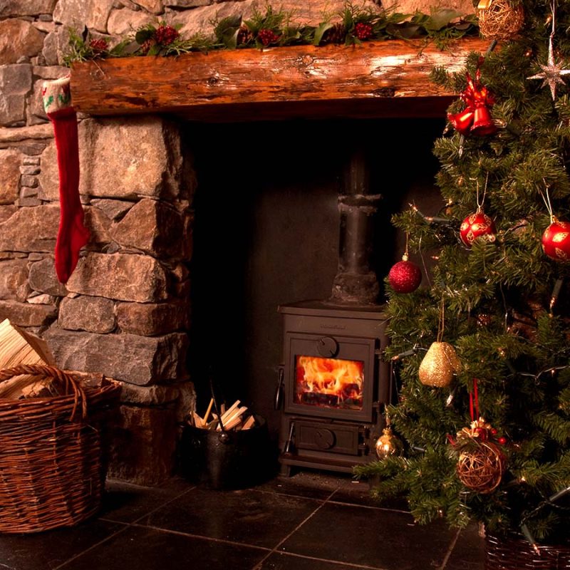 A festive fireplace with a roaring fire and Christmas tree at Blue Reef Cottages on the Isle of Harris in Scotland