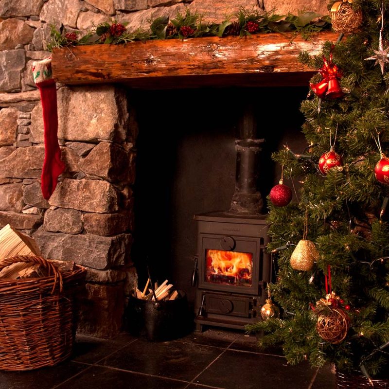A festive fireplace with a roaring fire and Christmas tree at Blue Reef Cottages on the Isle of Harris in Scotland